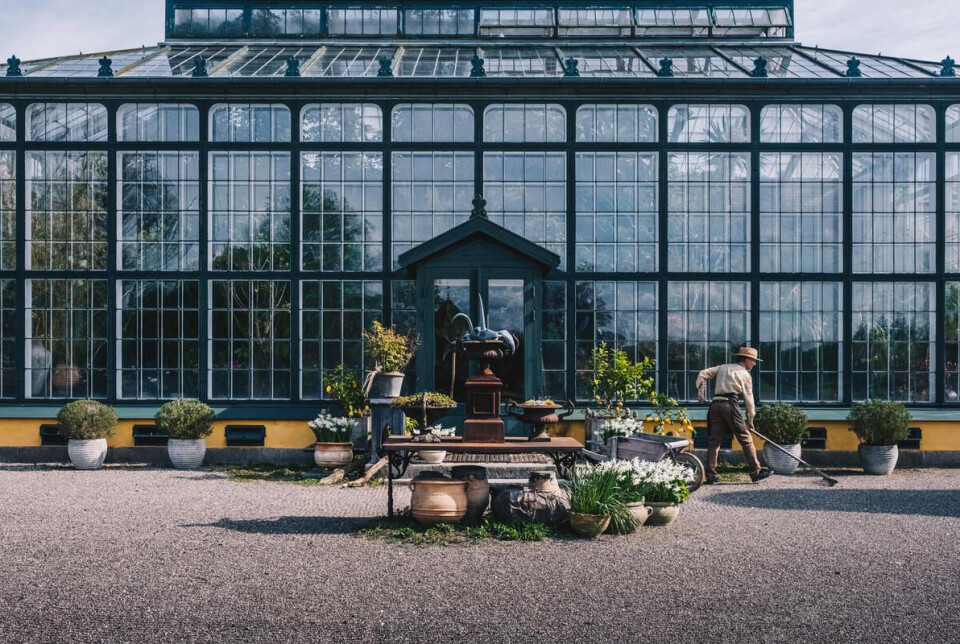 Paradehuset hos Gisselfeld Klosters.
Glashus med blomster og planter. Gartner går og fejer foran
