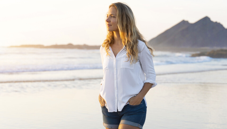 Kvinde går på strand i skjorte og shorts