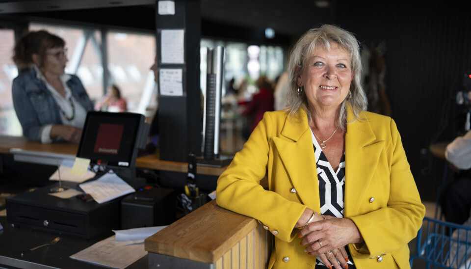 Lonnie fra 'Hotel Romantik' står i en gul jakke i en bar og smiler.