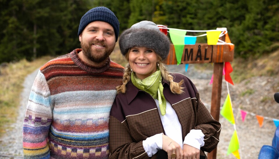 Sofie Linde og Joakim Ingversen smiler til kameraet, mens de står i naturen i 'Hotel Romantik'. De har begge huer på.