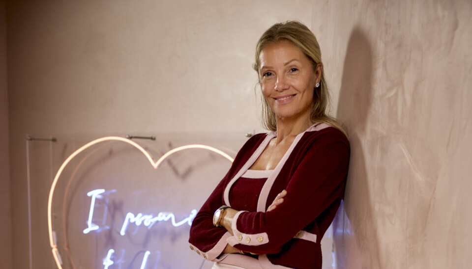 Caroline Fleming står op ad en væg med armene over kors og smiler ind i kameraet.