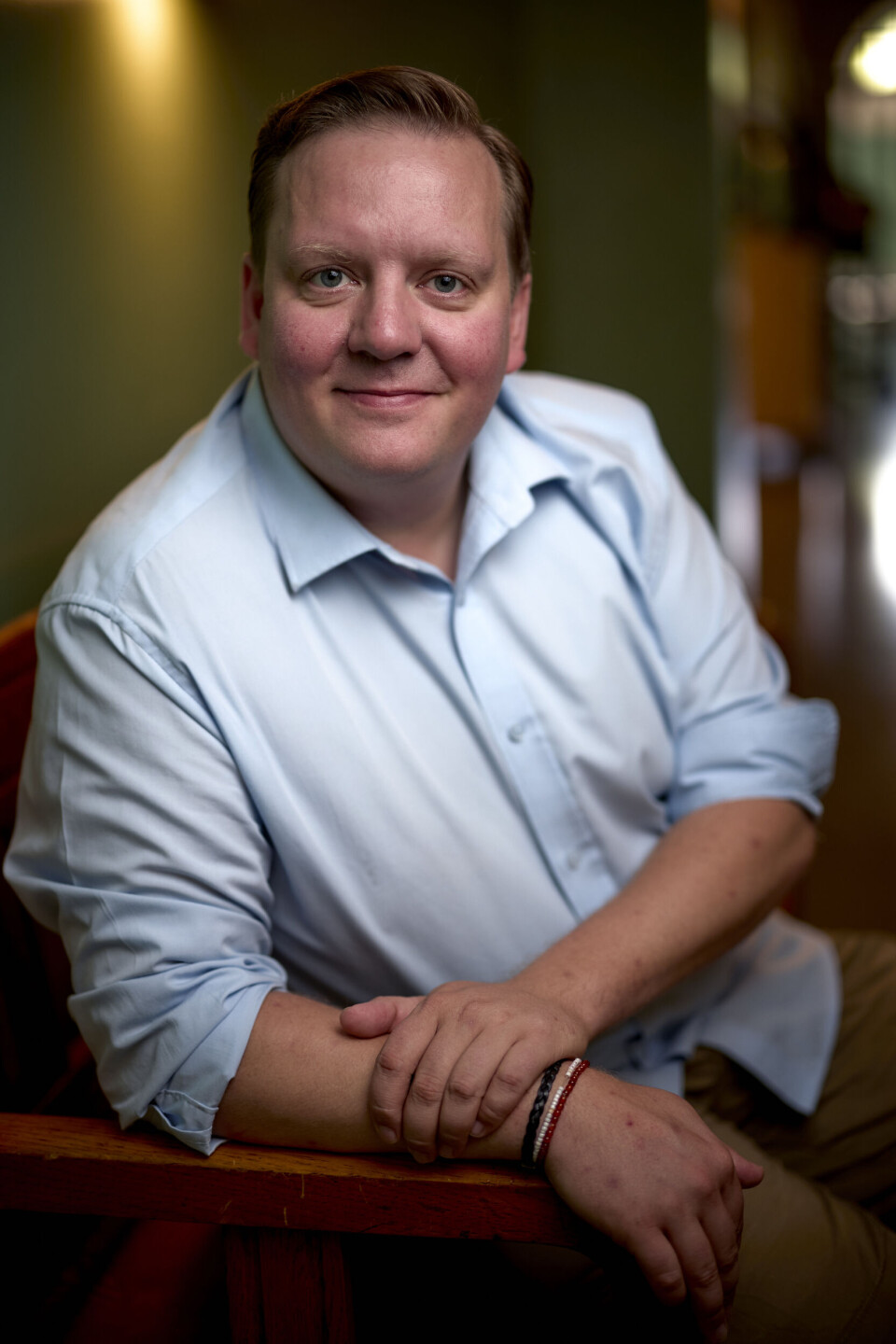 Jesper Ole iført en blå skjorte og siddende i en stol. Han smiler ind i kameraet.