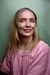 Portræt af Neel Rønholt iført en lyserød skjortebluse. Hun smiler ind i kameraet.