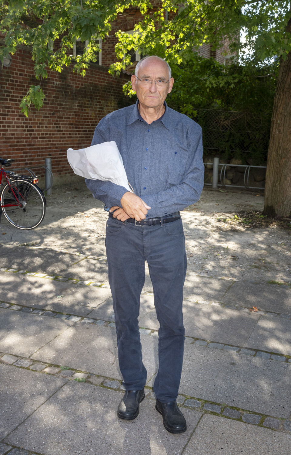 Holder en buket blomster og er iklædt en blå skjorte.