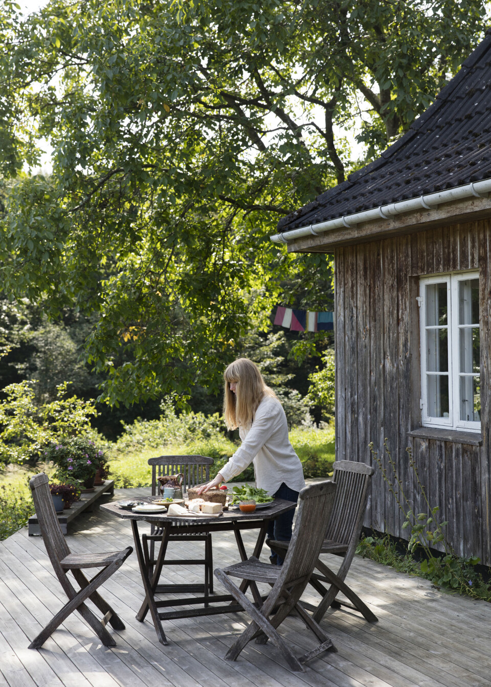 Træterrassen er bådebyggeren Birgers værk og løber langs øst- og nordsiden af huset. Den er skøn at spise frokost på, især når brødet er bagt med egne æg og det grønne høstet kort forinden. Flagene, der anes i baggrunden, er fra et kunstprojekt af et familiemedlem