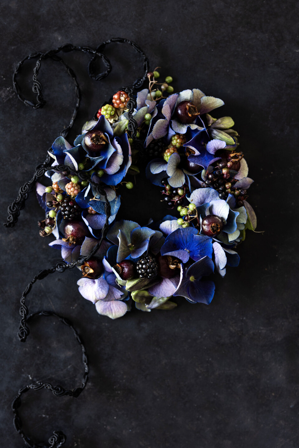 Frugt i kransen: Brombær, hyld og hyben er fine i en krans sammen med hortensia. Form en ring i kraftig ståltråd, ca. 10 cm i diam. Sno blomstertape om, inden du fastgør blomstertråden. Saml et lille bundt hortensiaer og frugt, og bind det til kransen. Fortsæt med en til to planter ad gangen. Saml kransen ved at skjule de sidste stængler under de første blomster. Hæft ende, og sæt bånd i.