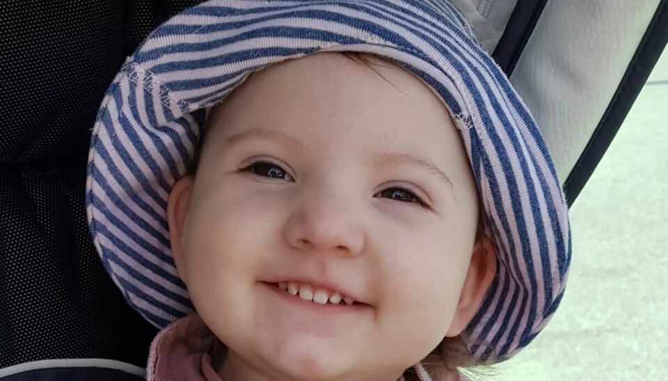 Lille Mina sidder med solhat og smiler