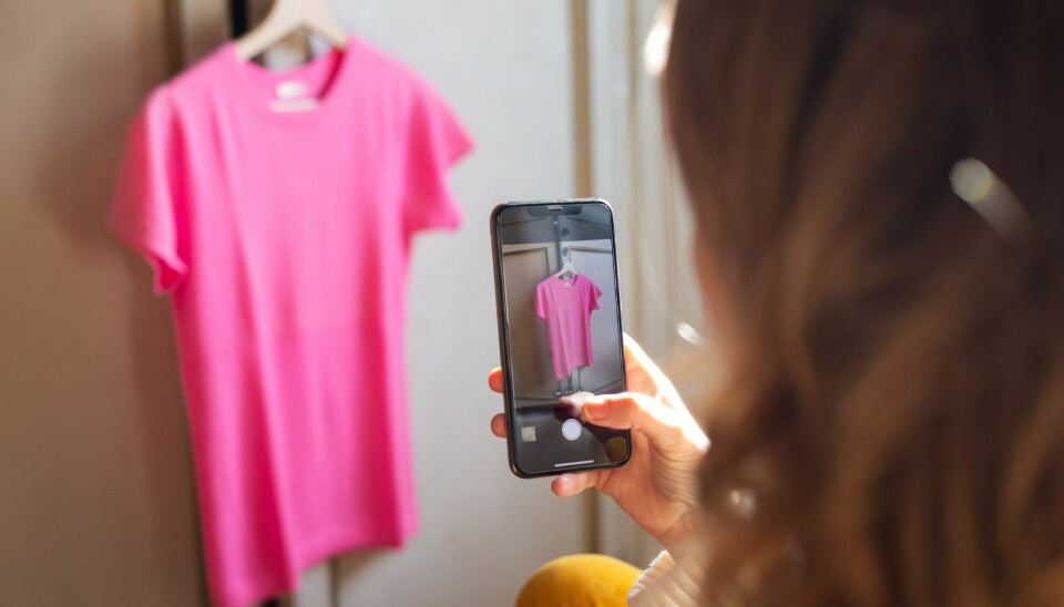 På billedet ses en kvindehånd, som holder en telefon. Hun er ved at tage et billede af en pink t-shirt, som hænger på en tøjbøjle.