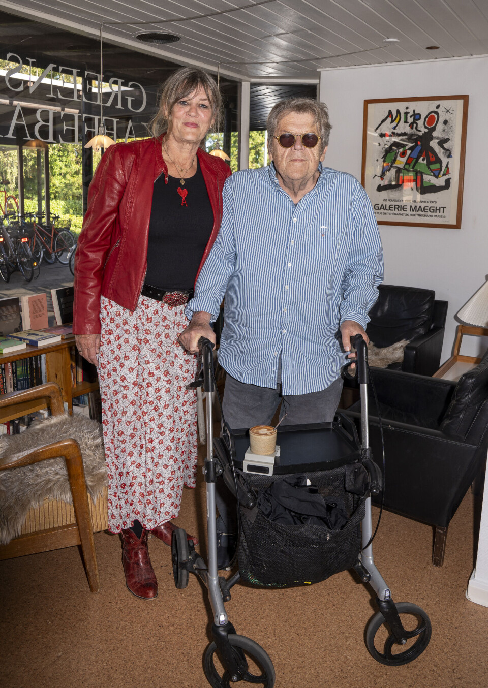 Noller står ved sin rollator og med sin hustru, klædt i rødt, ved sin side.