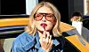 Gigi Hadid sidder med hovedet ud af en taxa. Hun er ved at tage en lyserød lipgloss på.