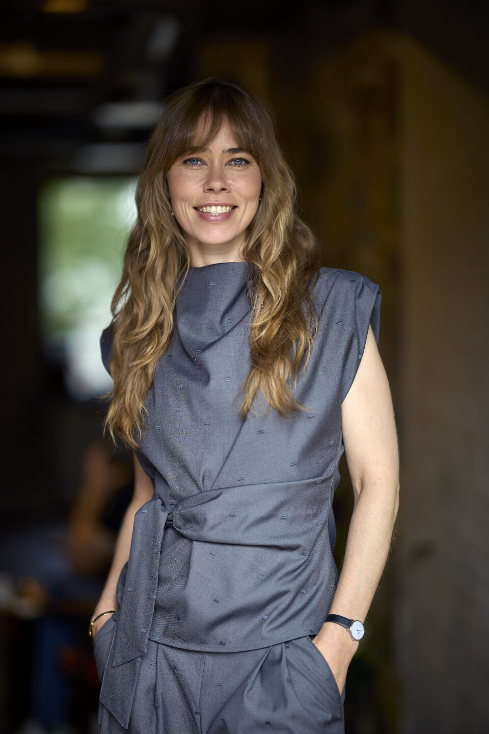 Birgitte med hænderne i lommerne i et gråt sæt med bindebånd.