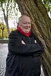 Bjarne Henriksen læner sig op ad et træ med et rødt halstørklæde på.
