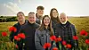 De seks nye landmænd står på en mark side om side med blomster i forgrunden.