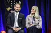 Kronprins Haakon og kronprinsesse Mette-Marit sidder side om side på en scene med mørk blå baggrund.