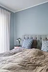 Soveværelse med blå væg, polstret sengegavl og sengetøj i neutrale farver