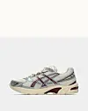 Asics-sneaker i sølv med bordeaux detaljer set fra siden mod neutral baggrund.