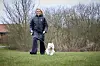 Mona Juul går tur med hunden Ludvig på en græsplæne foran nøgne buske