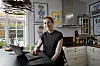 Helle Hirshals sidder med laptop ved køkkenbord i lyst hjem med plakater på væggen.