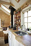 Lille køkken og ophjørn i træbeklædt tiny house med vindue og brændeovn.
