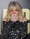 Skuespiller Goldie Hawn i mønstret kjole holder hænderne op foran ansigtet på en rød løber.