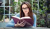 En kvinde sidder ude i sin have og læser i en bog.
