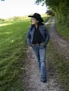 Kvinde i denim og cowboyhat går på en grusvej ved en grøn mark.