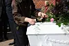 Person lægger blomst på hvid blomsterpyntet kiste ved udendørs begravelse
