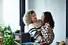 Young girl with curly hair being held by cheerful mature woman, bonding, love, care, togetherness