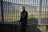 Fængselsbetjent i sort uniform går og taler i telefon foran et højt hegn.