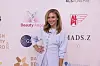 Kvinde i lyseblå kjole poserer foran sponsorvæg ved Beauty Awards 2026.