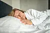 Moden kvinde sover på siden i en hvid seng med hvid pude og morgenkåbe.