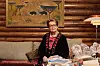 Ghita Nørby omgivet af bøger i stue med trævæg og stort maleri bagved.