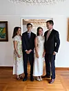 Fire personer i formelt tøj står sammen i en lys stue med trægulv og kunst på væggene.