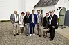 Konfirmand i blå jakkesæt står med familie foran hvid landsbykirke.