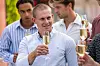 Flere unge mænd står udendørs og skåler med fyldte champagneglas.