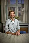 Magnus Haugaard sidder smilende ved et bord foran et vindue i et pressemødelokale.