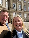 To personer tager en selfie foran Amalienborg Slot i solskin med garder i baggrunden.
