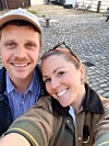 Smilende par tager selfie på en brostensbelagt gårdsplads udendørs.