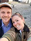 Smilende par tager selfie på en brostensbelagt gårdsplads udendørs.