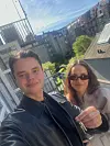 Unge mand og kvinde står på altan og holder en nøgle foran bybygninger i solskin.