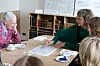 Personer ved bord studerer arkitekttegning med kaffekopper og bøger i baggrunden