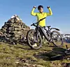Terrengsyklist i gul jakke står ved steinvarde på fjelltopp med elsykkel
