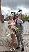 Brudepar står på brosten i byen, bruden med buket og hvid kjole, gommen i lysegråt jakkesæt.