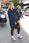 Gravid kvinde i denimjakke og træningstøj står på en travl by-gade i solskin.