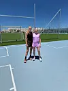 Rikke Holm-Nielsen og Bettina Møller står på en lys blå sportsbane foran et hegn og en grøn fodboldbane.