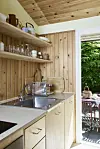 Lyst træbeklædt køkken med stålvask og åben dør til terrasse