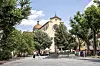 Historisk kirke og springvand på solrig italiensk plads med træer og mennesker.