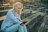 Eftertænksom kvinde med høretelefoner om halsen ser ned på sin smartphone på en tom tribune