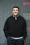 Havshen Nabaz står smilende foran en Netflix-fotovæg ved en premiereevent.