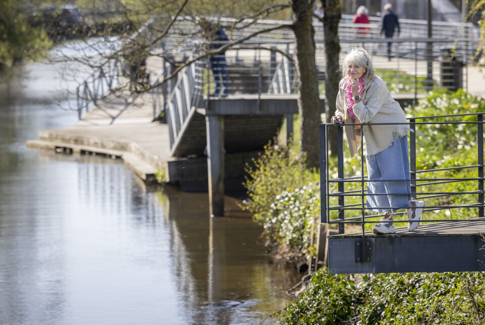 Billede 4 - Jena Krogslykke læner sig mod et rækværk ved en åpromenade omgivet af forårsgrønt.